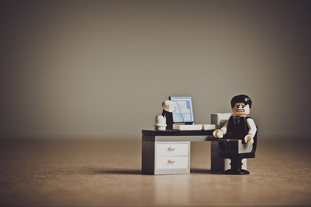 A lego man with a sad face sitting in front of an office desk